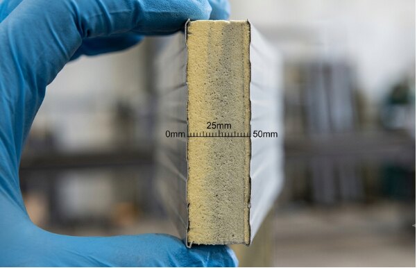 Cut section of a wall panel held against a scale, showing the 50mm insulated core between two steel skins